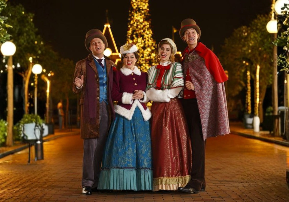 Oldtime carolers performing Christmas songs on a lamplit street in front of a grand Christmas tree