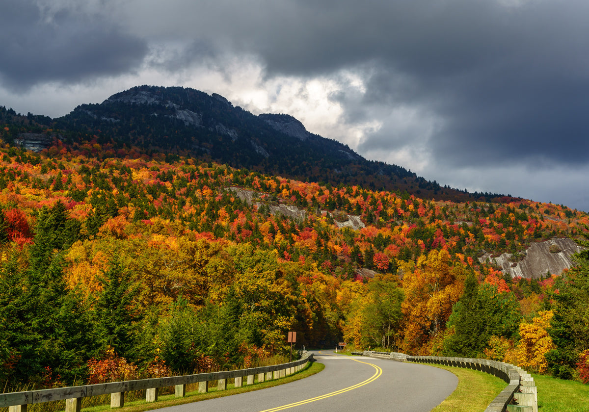 Tour of the New Hampshire highway showcasing autumn landscape with colorful trees and a mountain under a cloudy sky.