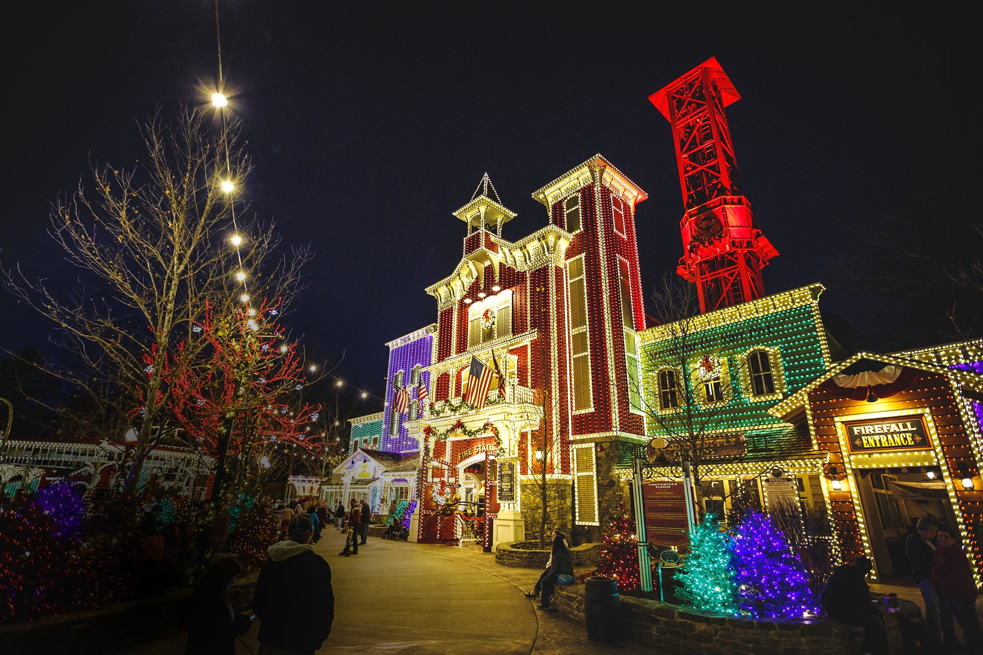 Touring a festive nightime scene with brightly lit holiday buildings, string lights, bare trees, in Branson Missouri.
